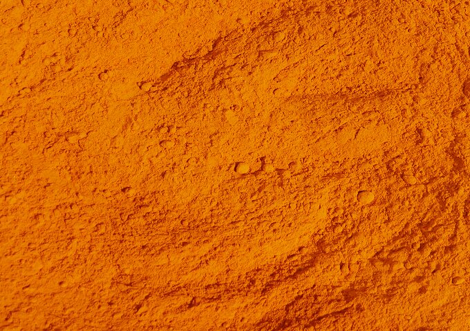 Strukturierte Nahaufnahme von leuchtend orangefarbenem Gewürzpulver – feine, trockene Oberfläche mit leichter Körnung, symbolisch für Gewürze oder Streuprodukte in funktionalen Verpackungssystemen.
