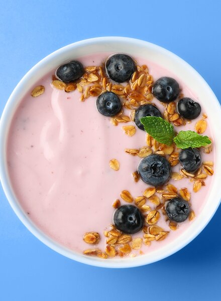 Schale mit Joghurt, Blaubeeren und Granola auf hellblauem Hintergrund – Symbolbild für frische Lebensmittel und Verpackungslösungen von säntis packaging.