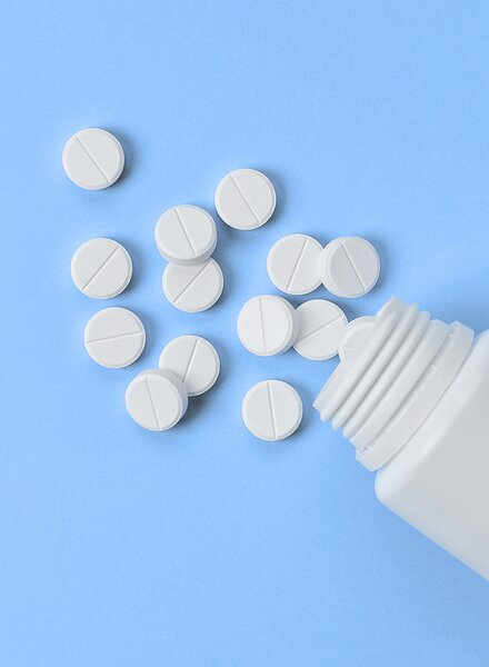 Weisse Kunststoffdose mit herausgefallenen Tabletten auf hellblauem Hintergrund – Symbolbild für hygienische und präzise Verpackungslösungen im Healthcare-Bereich von säntis packaging.