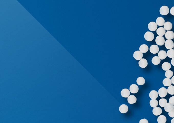 Weisse Kunststoffgranulate auf blaue Fläche – Symbolbild für Rohmaterial, Nachhaltigkeit und Materialkompetenz in den Folienlösungen von säntis packaging.