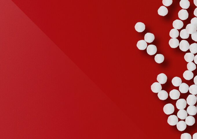 Weisse Kunststoffgranulate auf rote Fläche – Symbolbild für Rohmaterial, Nachhaltigkeit und Materialkompetenz in den Folienlösungen von säntis packaging.