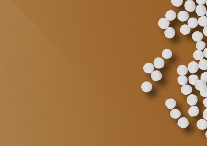 Weisse Kunststoffgranulate auf braune Fläche – Symbolbild für Rohmaterial, Nachhaltigkeit und Materialkompetenz in den Folienlösungen von säntis packaging.