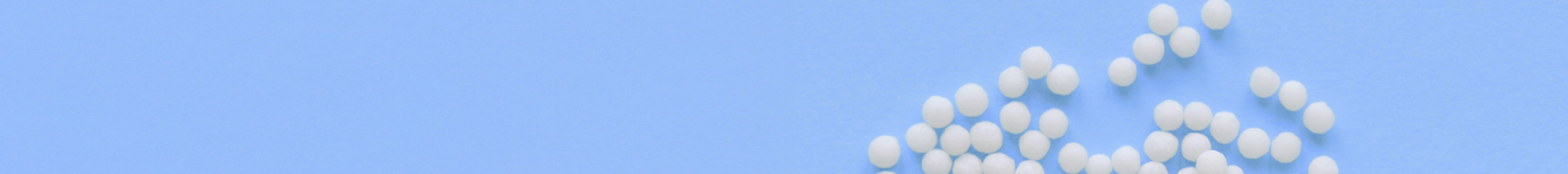 Weisse Kunststoffgranulate auf hellblauem Hintergrund – Symbolbild für Materialvielfalt, Qualität und Präzision in den Kunststofflösungen von säntis packaging.