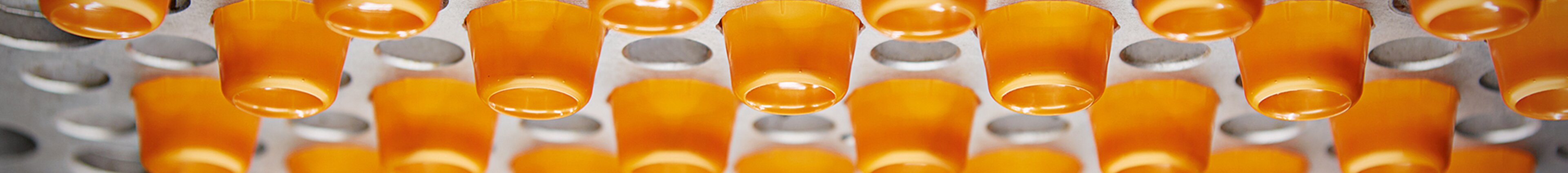 Tiefziehform mit orangefarbenen Kunststoffbechern – präzise und effiziente Thermoform-Technologie von säntis packaging.