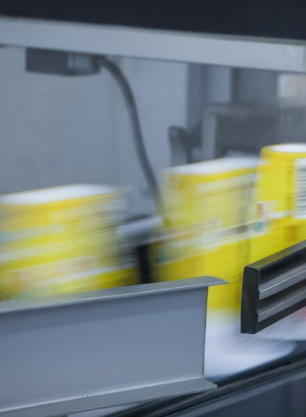 Produktionslinie mit gelben Kunststoffbechern im Sleeve-Prozess – vollflächige Schrumpffolien-Dekoration von säntis packaging.