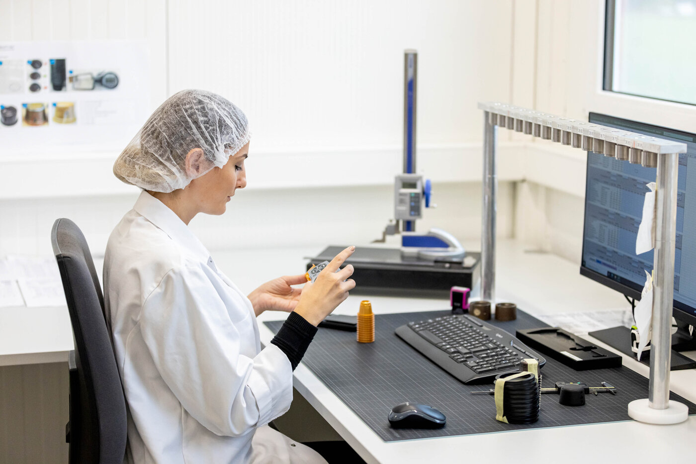 Mitarbeiterin im weissen Laborkittel und Haarnetz prüft Kunststoffkomponenten im Prüflabor von säntis packaging – Qualitätskontrolle und Bemusterung mit digitaler Dokumentation.