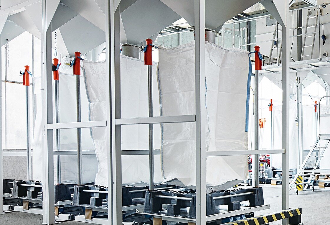 Grosse weisse Mahlgutsäcke unter Materialtrichtern in der Produktion von säntis packaging – Teil des Leanmanagement-Prozesses für effiziente, ressourcenschonende Materialnutzung und Recycling.