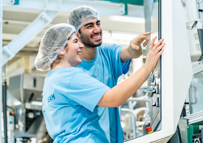 Zwei Lernende bei säntis packaging bedienen gemeinsam ein digitales Steuerungspanel einer Produktionsmaschine – Ausbildung in moderner Kunststoffverarbeitung mit Fokus auf Technik und Teamarbeit.