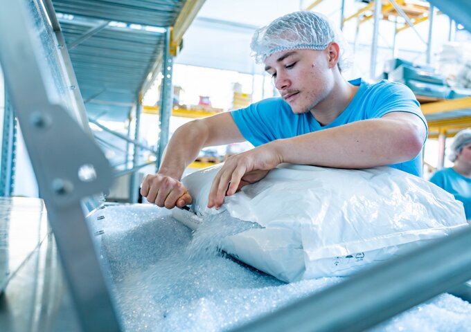 Lernender bei säntis packaging öffnet einen Sack mit Kunststoffgranulat und schüttet das Material in eine Produktionsanlage – praktische Tätigkeit in der Ausbildung zum Kunststofftechnologen.