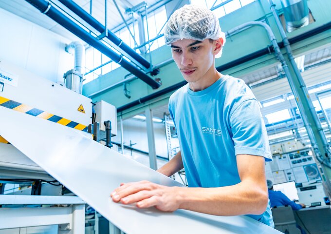 Lernender bei säntis packaging prüft sorgfältig eine Kunststofffolie an einer Produktionsmaschine – praxisorientierte Ausbildung in moderner Kunststoffverarbeitung.