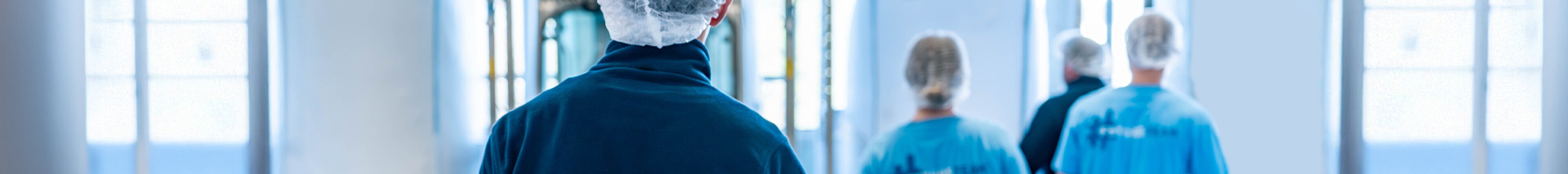 Mitarbeitende von säntis packaging mit Haarnetz und blauer Arbeitskleidung gehen durch die Produktionshalle – Symbolbild für Teamarbeit, Sicherheit und moderne Arbeitsumgebung.