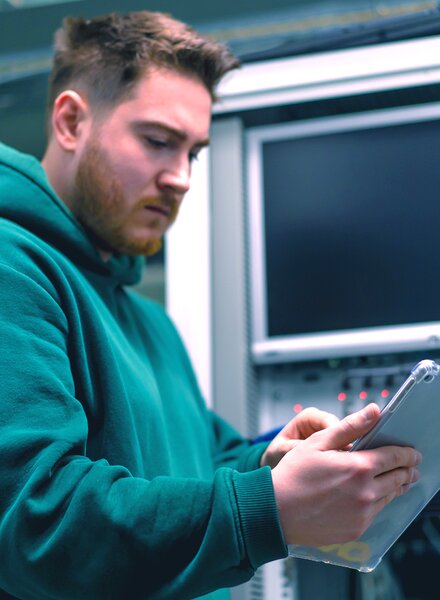 Student im technischen Umfeld arbeitet mit Tablet an einem Serversystem – praxisnahes Lernen und Digitalisierung bei säntis packaging im Rahmen eines Studiums oder Praktikums.