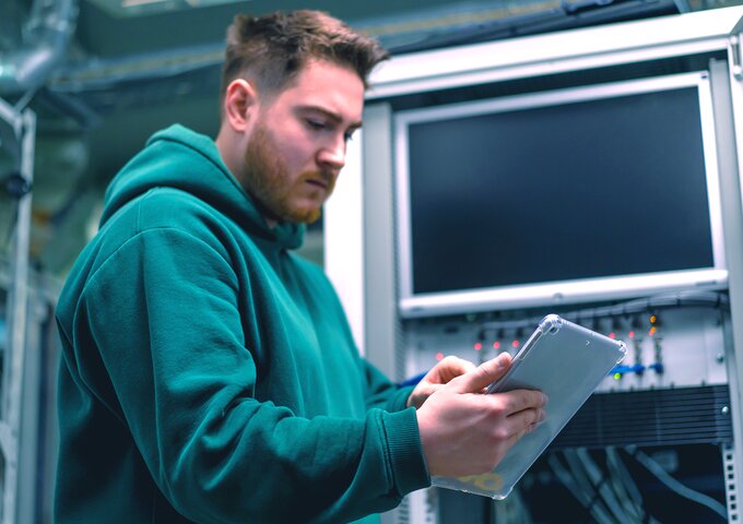 Student im technischen Umfeld arbeitet mit Tablet an einem Serversystem – praxisnahes Lernen und Digitalisierung bei säntis packaging im Rahmen eines Studiums oder Praktikums.