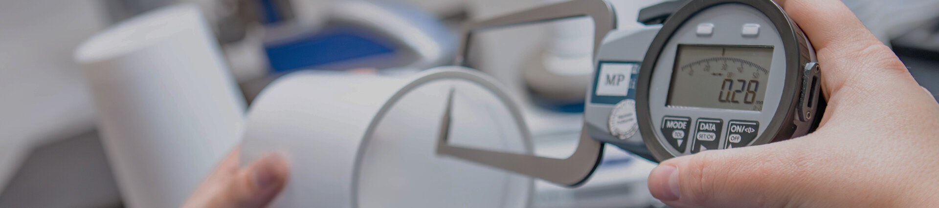 Mitarbeiterin misst die Wandstärke eines Kunststoffbechers mit einem digitalen Messgerät – Qualitätsprüfung und Präzisionskontrolle bei säntis packaging.