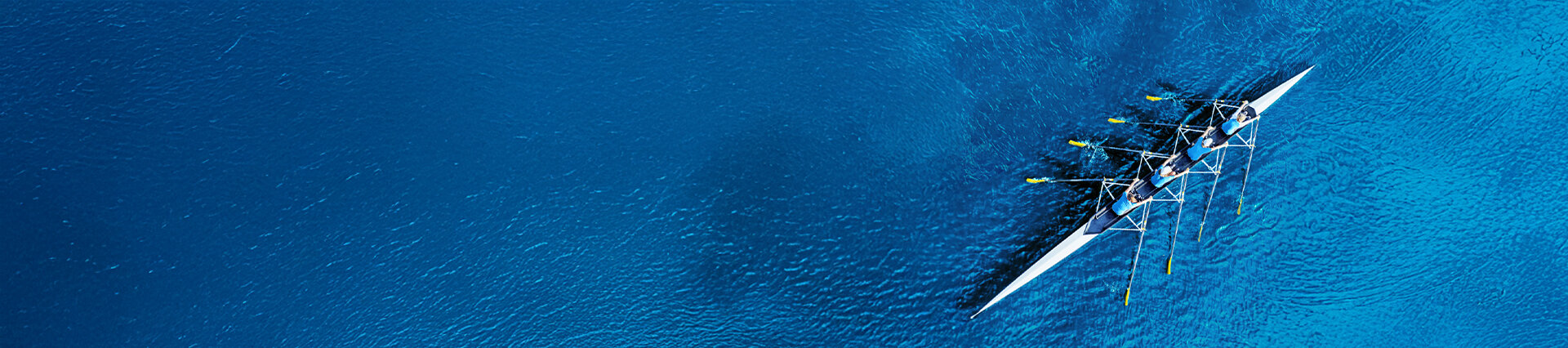 Luftaufnahme eines Ruderteams auf tiefblauem Wasser – Symbol für Teamwork, gemeinsame Richtung und den Start in die berufliche Zukunft bei säntis packaging.