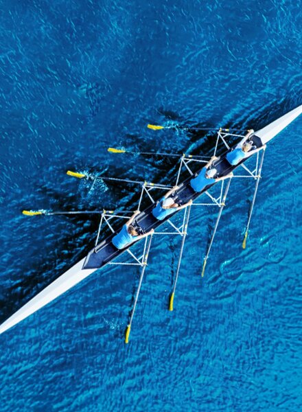 Luftaufnahme eines Ruderteams auf tiefblauem Wasser – Symbol für Teamwork, gemeinsame Richtung und den Start in die berufliche Zukunft bei säntis packaging.