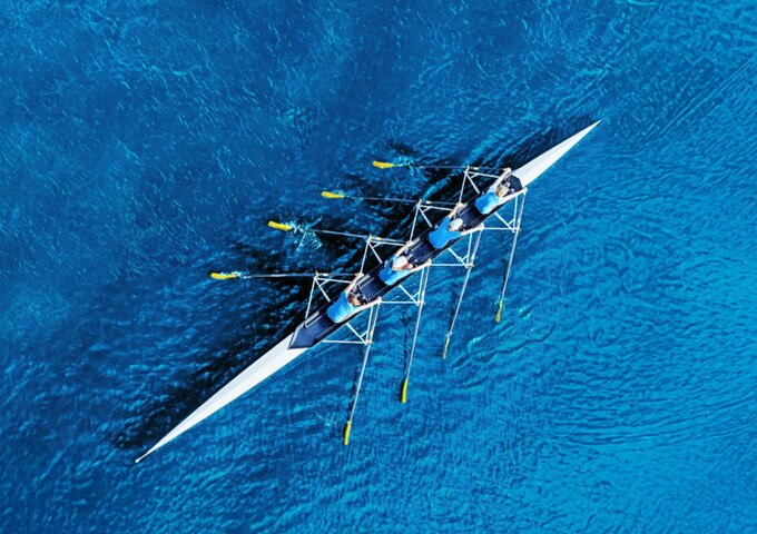 Luftaufnahme eines Ruderteams auf tiefblauem Wasser – Symbol für Teamwork, gemeinsame Richtung und den Start in die berufliche Zukunft bei säntis packaging.