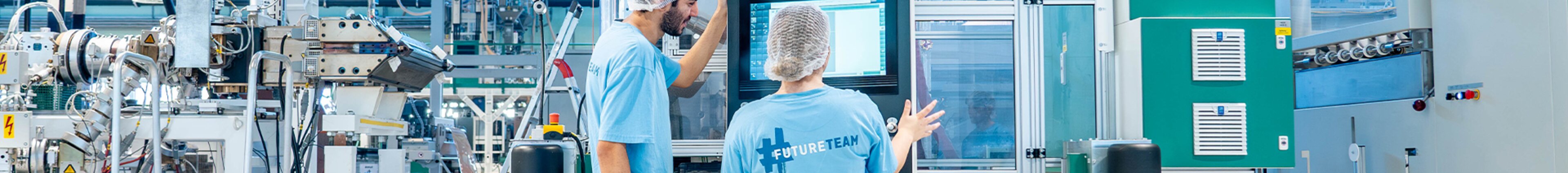 Zwei Mitarbeitende von säntis packaging in Produktionshalle vor einem Touchscreen – symbolisiert Teamarbeit, Technologiekompetenz und moderne Arbeitsumgebung im Unternehmen.