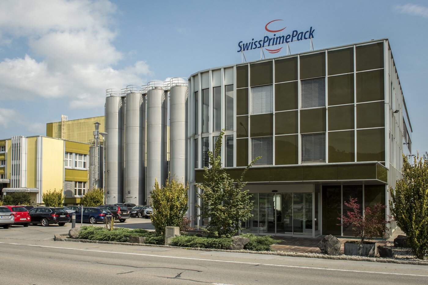 Aussenansicht des ehemaligen Firmengebäudes der Swiss Prime Pack AG in Altstätten mit markantem Silokomplex und Glasfassade – Symbol für die abgeschlossene Integration in die säntis packaging ag im Jahr 2024.