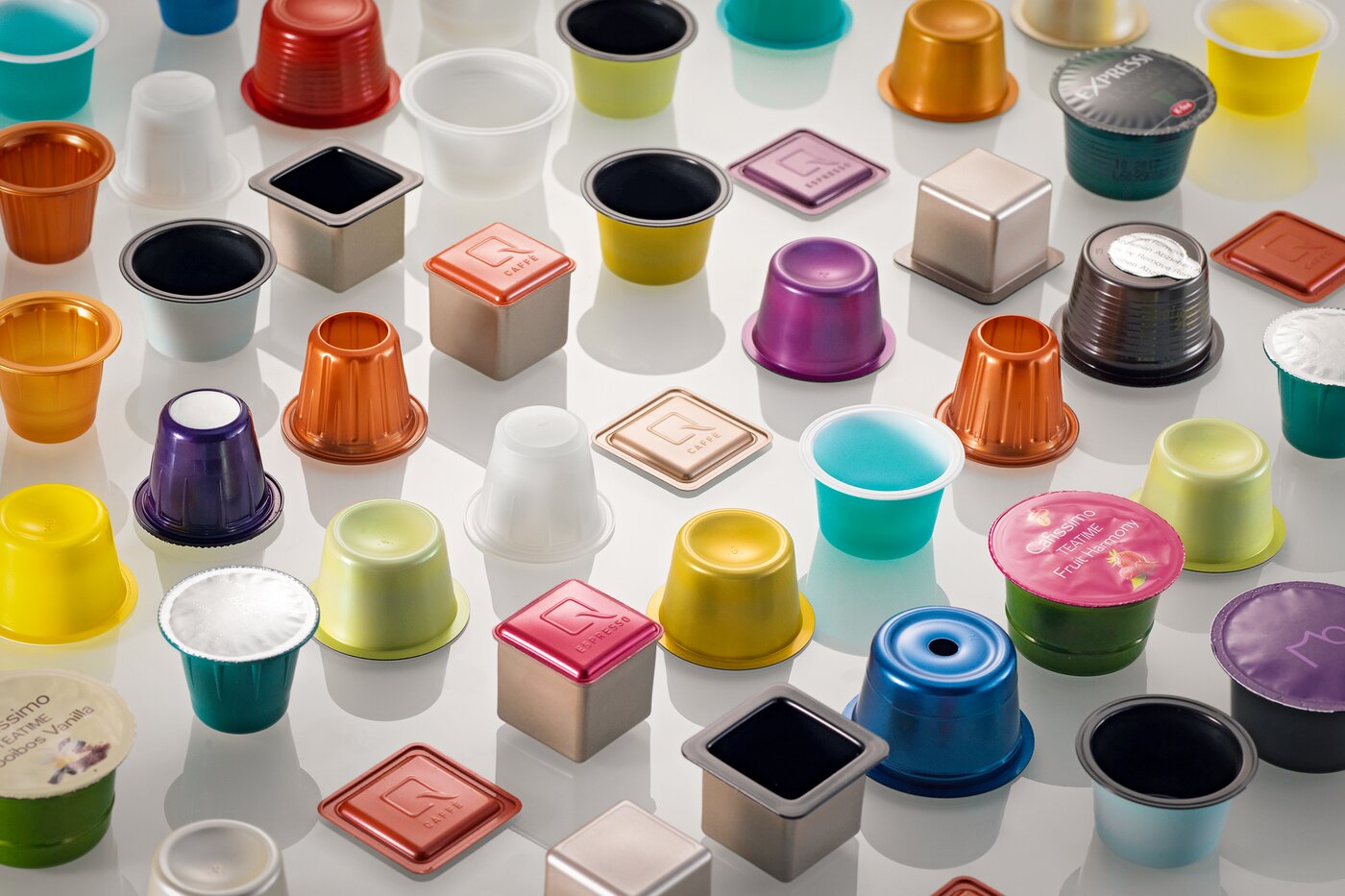 Vielfältige, bunte Kaffeekapseln in unterschiedlichen Formen und Materialien auf weissem Hintergrund – Sinnbild für die von SÄNTIS ab 1991 entwickelten barriereschützenden PP-EVOH-Kapseln, die den europäischen Markt nachhaltig prägten.