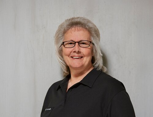 Porträt von Bea Kobler Bösch, HR-Sachbearbeiterin der säntis packaging ag – in schwarzem Poloshirt mit Firmenlogo, freundlich und authentisch vor hellem Hintergrund fotografiert.