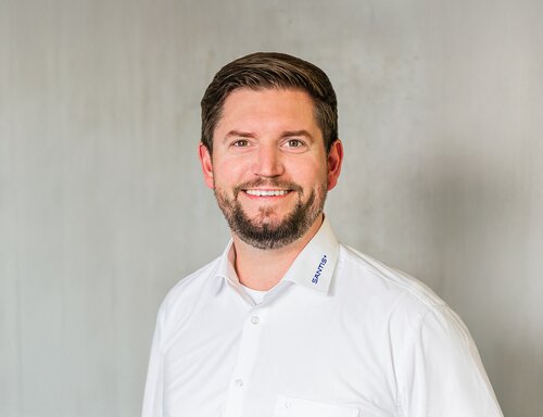 Porträt von Cornel Müntener, Head of Sales bei säntis packaging ag – in weissem Hemd mit Firmenlogo am Kragen, freundlich und professionell vor neutralem Hintergrund fotografiert.