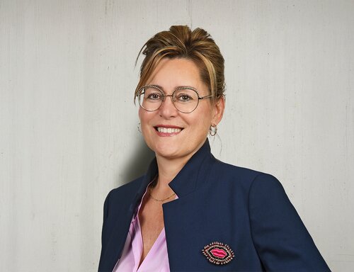 Porträt von Dr. Bettina Fleisch, Inhaberin und Chairwoman der säntis packaging ag – in dunkelblauem Blazer mit rosa Bluse, lächelnd und professionell vor hellem Hintergrund fotografiert.