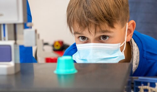 Junge Teilnehmer beobachtet aufmerksam eine grüne Kunststoffkapsel während der Qualitätsprüfung bei den Young-Tec-Days von Säntis Packaging.