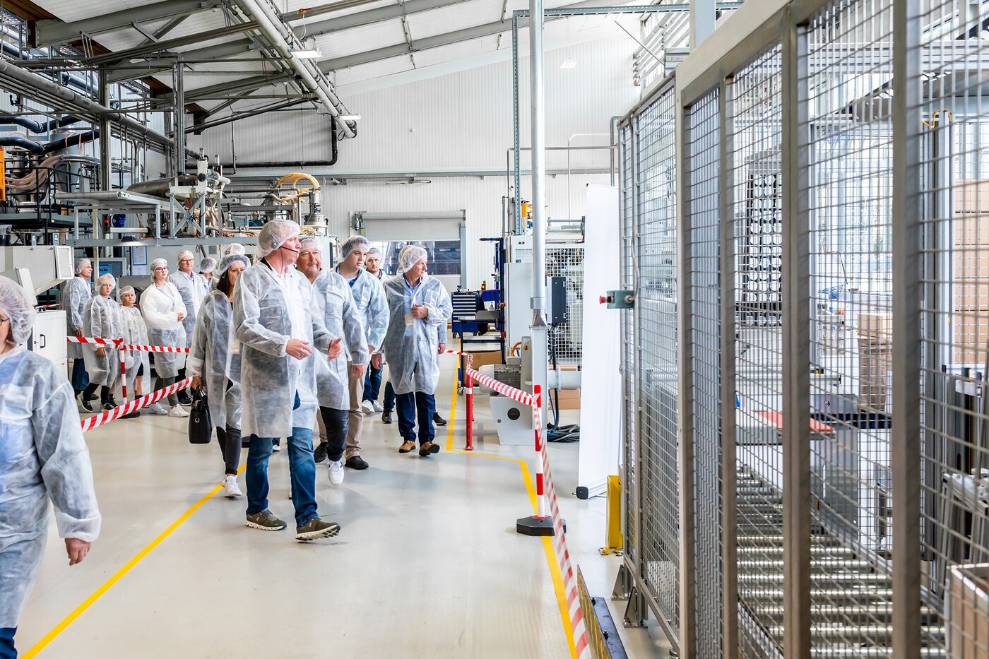 Besuchergruppe in Schutzkleidung bei einer Werksführung durch die Produktionshalle von Säntis Packaging in Rüthi – Einblick in moderne Spritzguss- und Verpackungstechnologien während der 100-Jahr-Feier.