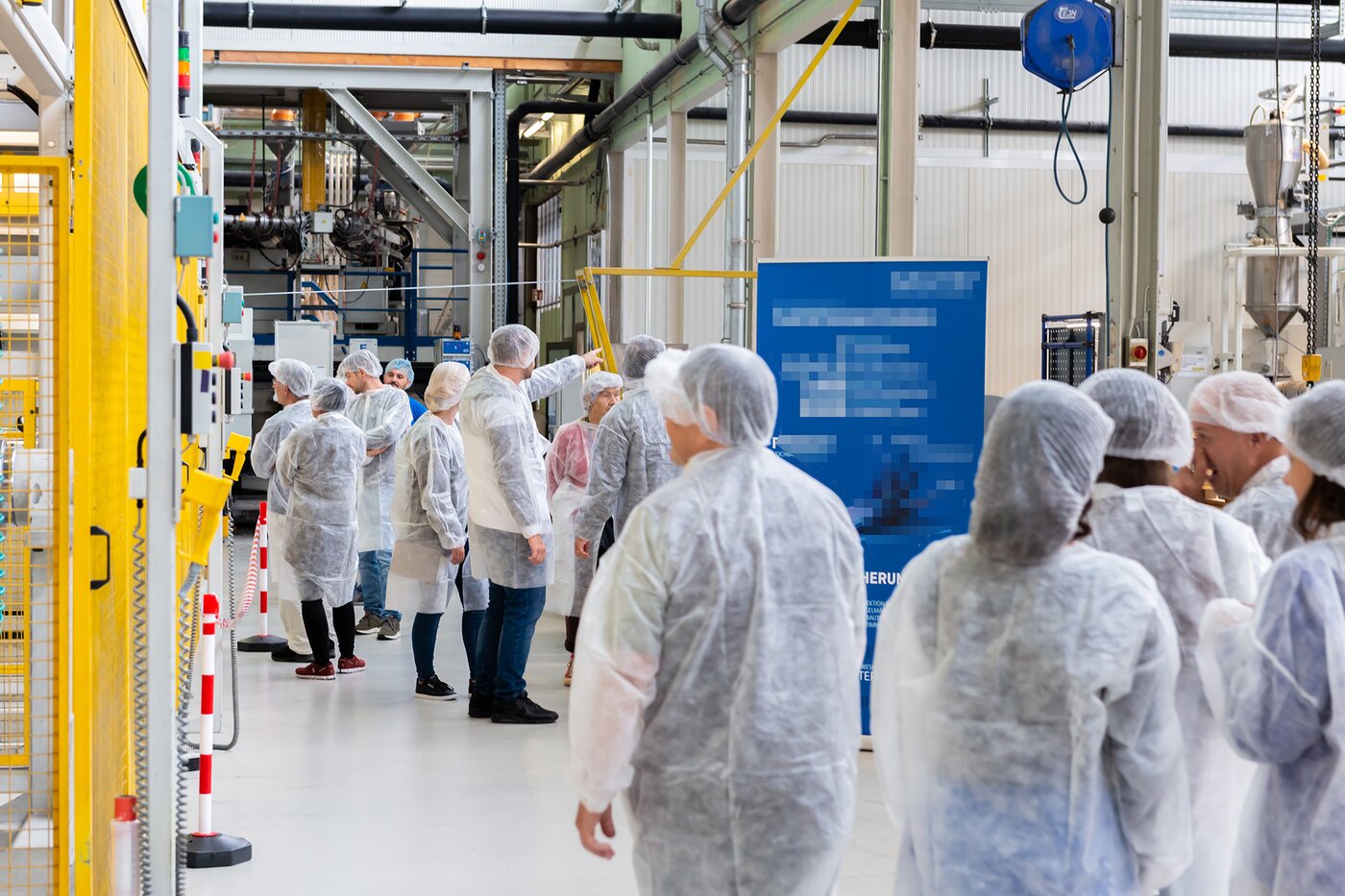 Besuchergruppe in Schutzkleidung besichtigt die Produktionsanlagen von Säntis Packaging – Einblick in Fertigungsprozesse und Technologie während des Tags der offenen Werkstore zum 100-jährigen Jubiläum.