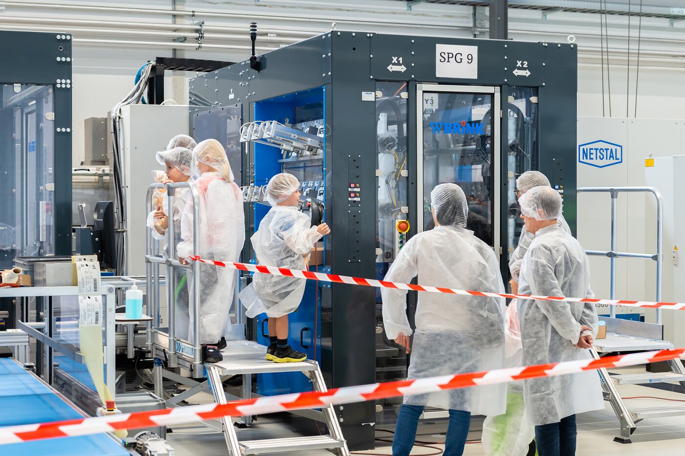 Familien und Besucher in Schutzkleidung betrachten eine Spritzgussmaschine bei Säntis Packaging – Demonstration moderner Produktionstechnologie während des Jubiläums-Tags der offenen Tür.