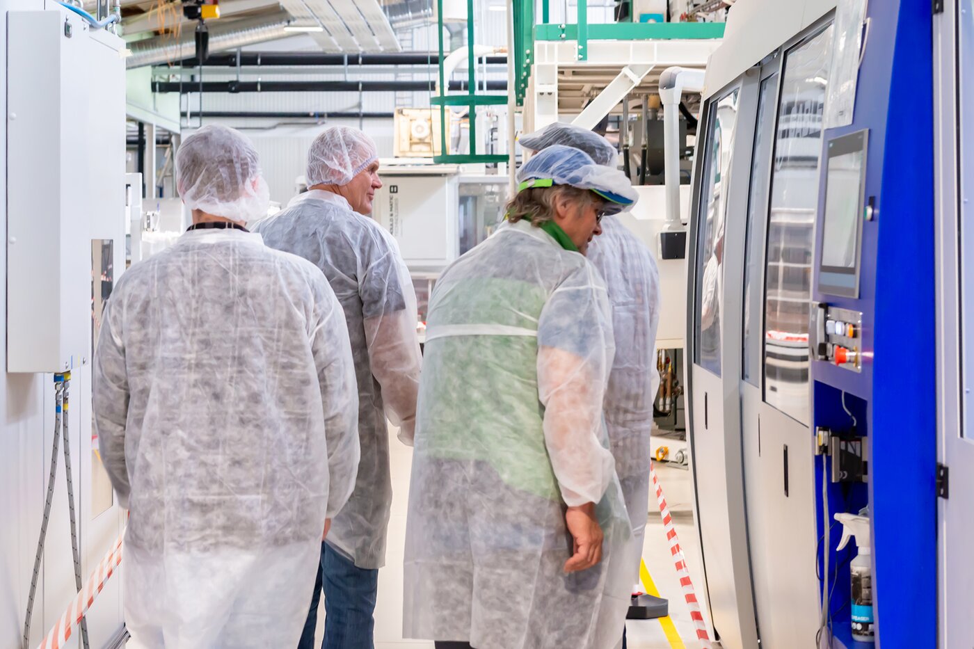 Besucher in Schutzkleidung besichtigen eine Produktionslinie bei Säntis Packaging – Einblick in moderne Maschinen und Fertigungsprozesse während der Jubiläumswerksführung.