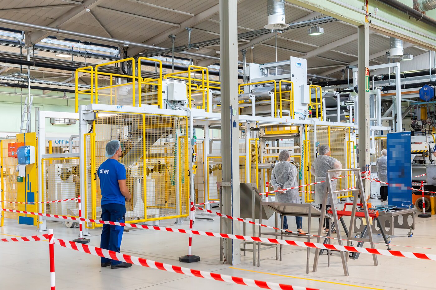 Mitarbeitende führen Besucher in Schutzkleidung durch den Produktionsbereich von Säntis Packaging und erklären Maschinen und Abläufe während des Jubiläumsrundgangs.