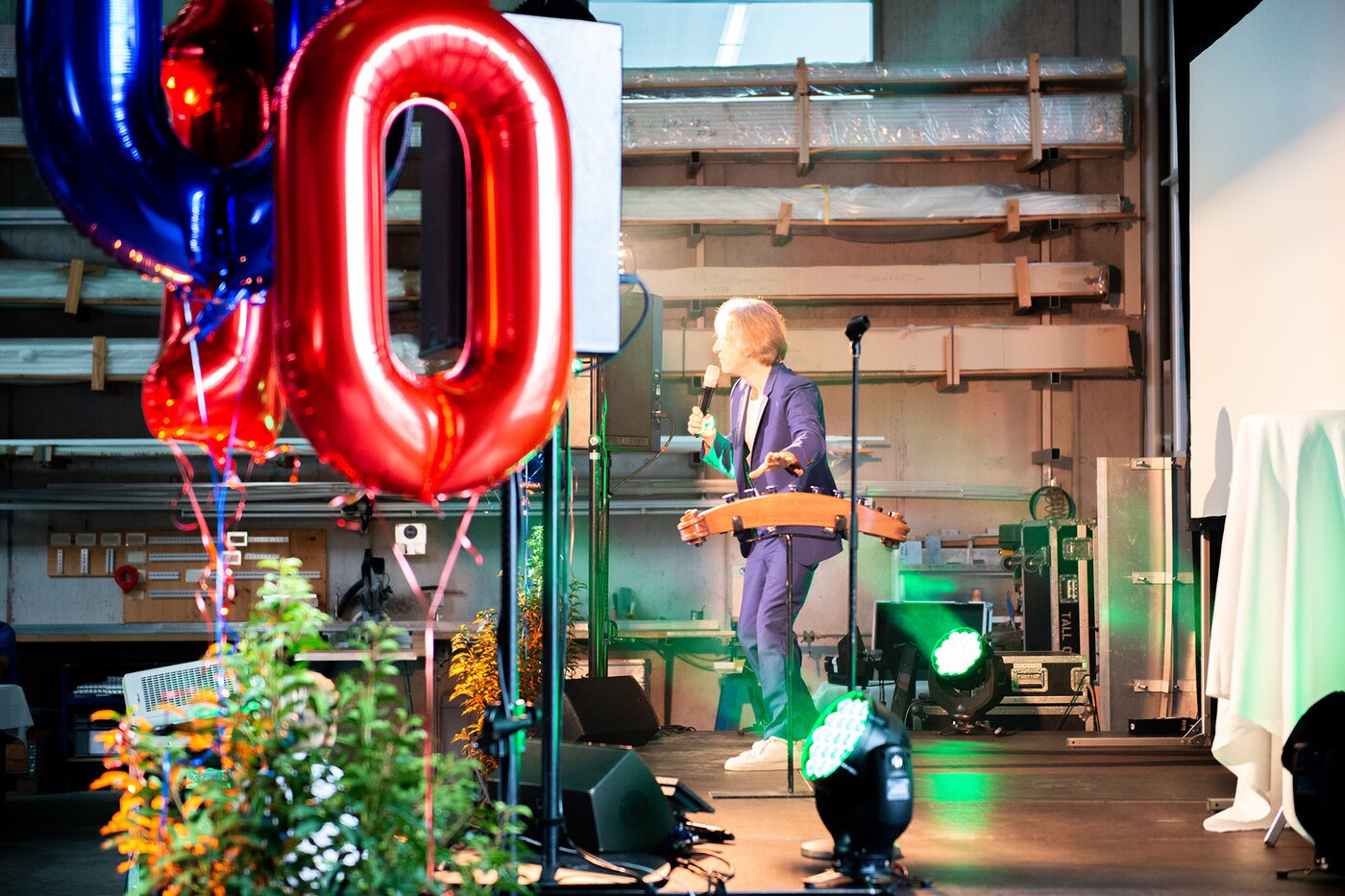 Bühnenauftritt mit Musiker und rotem Jubiläumsballon bei der 100-Jahr-Feier der SÄNTIS-Gruppe – festliche Atmosphäre mit Live-Performance und Beleuchtung im Firmengebäude in Rüthi.