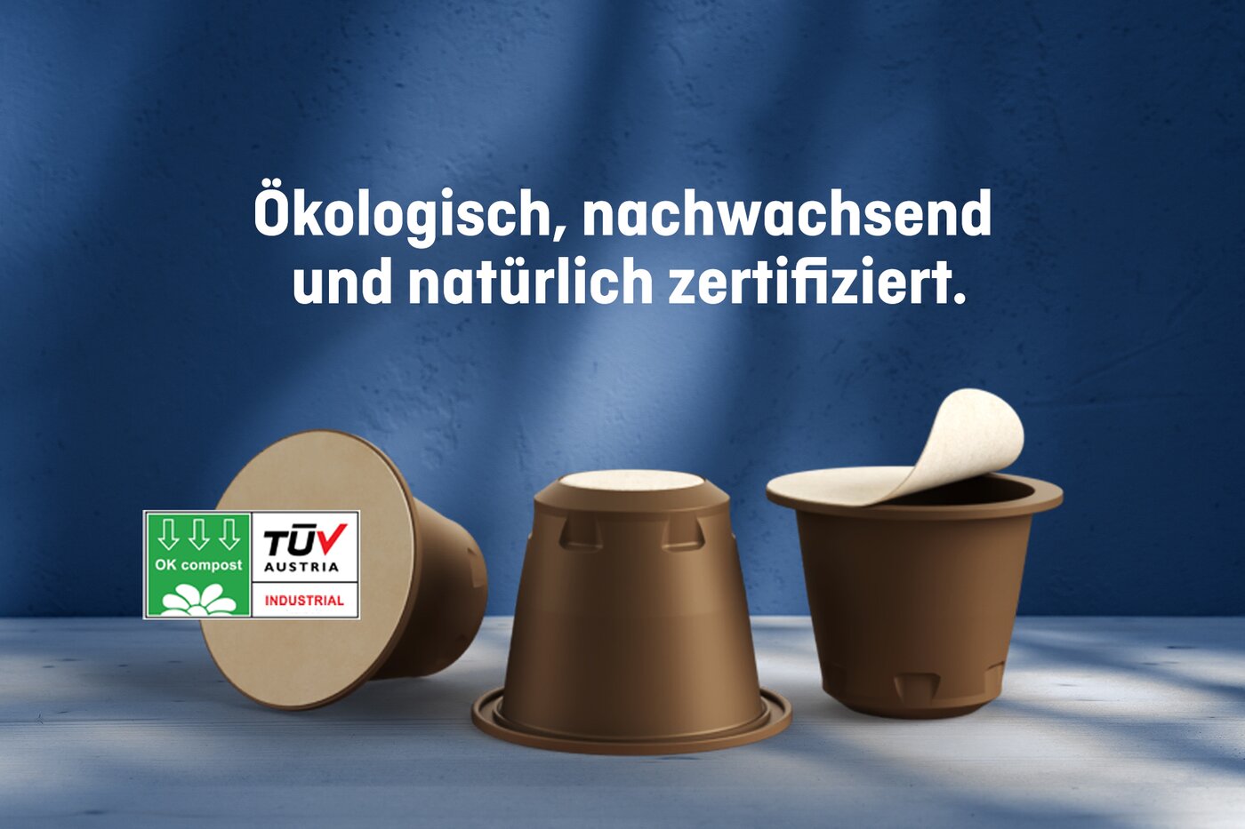 Drei braune, kompostierbare Kaffeekapseln mit TÜV-Austria- und OK-Compost-Zertifizierung, begleitet vom Schriftzug «Ökologisch, nachwachsend und natürlich zertifiziert» – Symbolbild für die nachhaltige NAT®Cap-Lösung von Säntis Packaging.